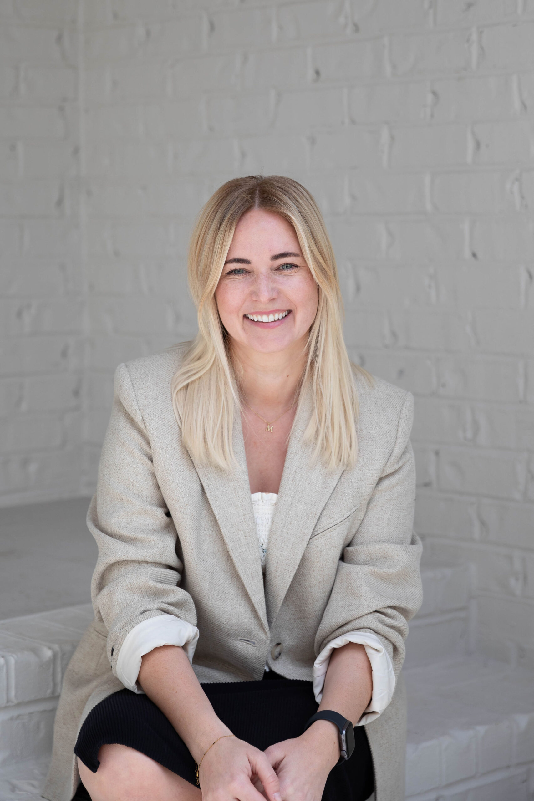 Melissa Baton, Founder of Prosperity Hive, seated against a white brick wall